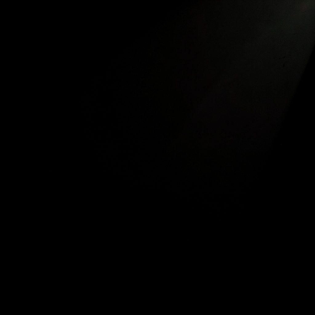 Dark low-key photograph of consumer electronics packaging in deep shadow, subtle coral accent glow
